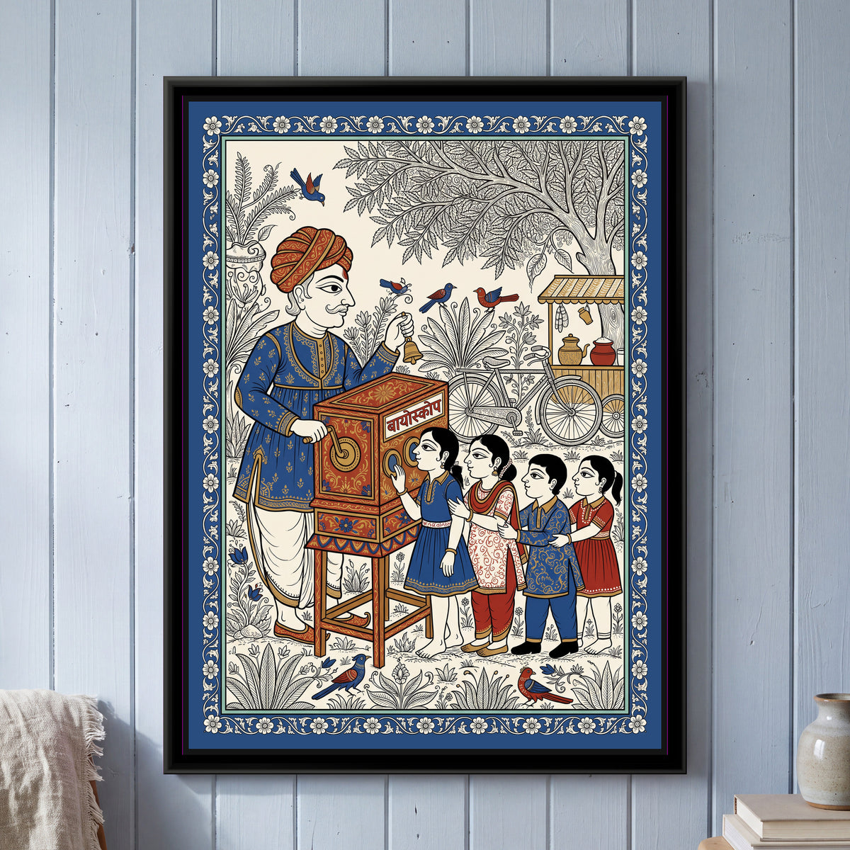 Phad Painting – Bioscope Wala - framed canvas print of an old bioscope man in an orange turban and blue kurta ringing a brass bell and turning the crank of a painted wooden bioscope box on legs, four children queued at the viewing windows, a bicycle and a tea stall under a big tree, birds, deep blue floral border, hung on a wall