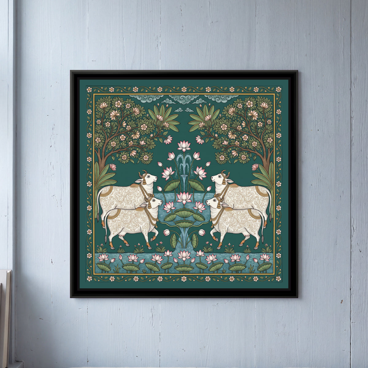 Pichwai Painting – Cows around a Lotus Pond - framed canvas print of four white cows with fine gold scroll patterns on their coats, gold bells and tassels, two on each side facing a central fountain of pink lotuses and green lotus leaves rising from blue water, two flowering trees with pink blossoms arching in from the corners, banana leaves, curling blue clouds at the top, a strip of lotus pond along the bottom, a deep green ground with a border of small pink flowers on a vine, hung on a wall