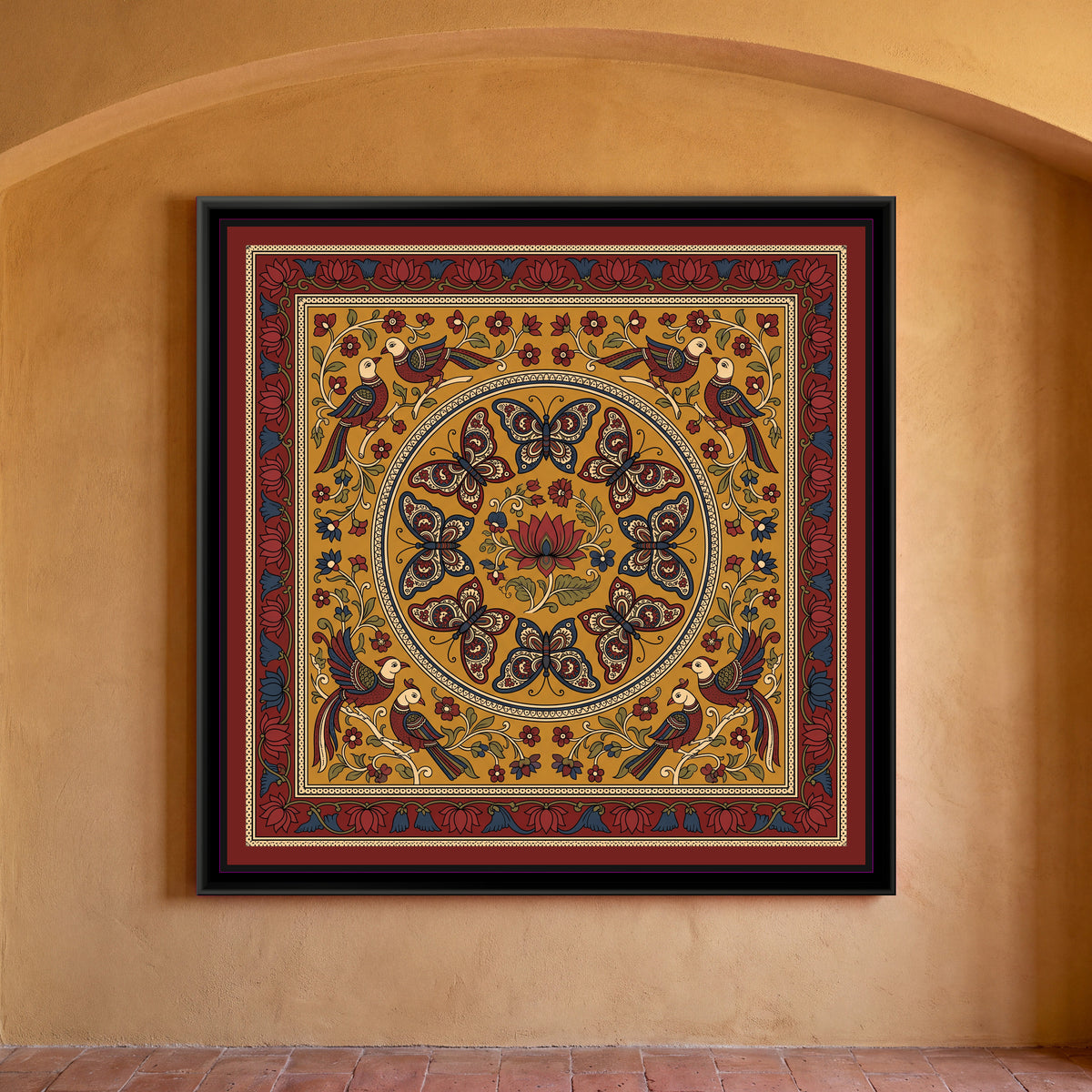 Kalamkari Painting – Butterfly Mandala - framed canvas print of eight butterflies with paisley-patterned wings in indigo, red and cream arranged in a ring around a single red lotus with leaves inside a large circular medallion, four pairs of long-tailed birds perched on cream branches in the corners among small red and blue flowers, all on a mustard yellow ground, inside a deep red border of red and blue lotuses, hung on a wall