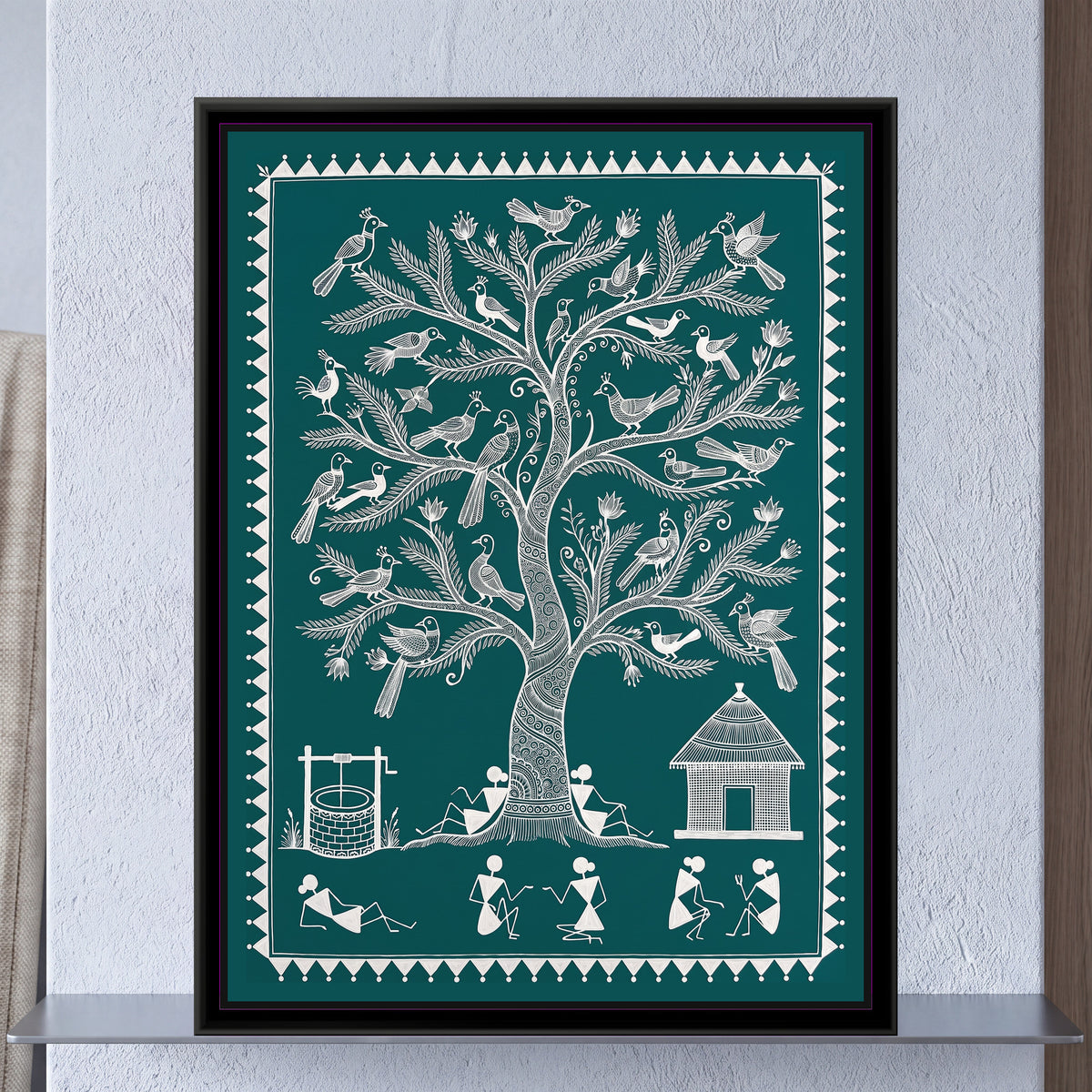 Warli Painting – Tree of Life with Birds – Deep Teal - framed canvas print of a tall Warli tree of life with a spiral-patterned trunk and feathery branches holding around thirty crested birds and small lotus buds, two villagers leaning against the trunk, a brick well with a winch on the left, a thatched hut on the right and a row of stick-figure villagers chatting and resting below, white line on a deep teal green ground inside a border of white triangles and dots, hung on a wall