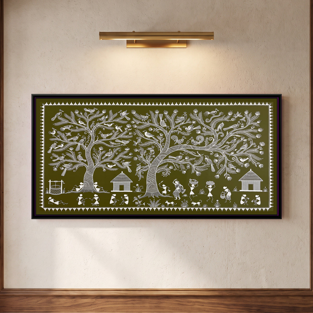 Warli Painting – Tree of Life Village Panorama - framed canvas print of a wide Warli panorama with two large trees full of crested birds and a rooster, a well and resting villagers on the left, three thatched huts, a dancing woman, women carrying baskets on their heads, a dog and a cat, small plants and seated pairs chatting along the ground, white line on an olive green ground inside a border of white triangles, hung on a wall