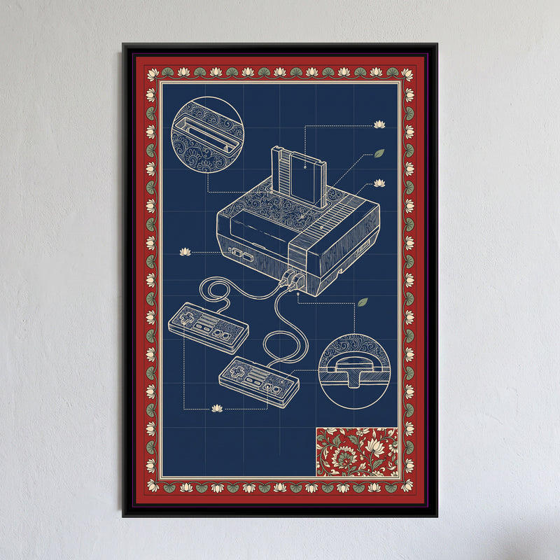 Kalamkari Blueprint – Retro Games Console - framed canvas print of a cream line drawing of a retro games console with a cartridge slotted in and two wired controllers on an indigo blueprint grid, its top covered in paisley swirls, circular close-ups of the cartridge slot and a controller button, dotted leader lines ending in small lotus and leaf motifs, a red border of cream lotuses and green leaves with a floral corner panel, hung on a wall