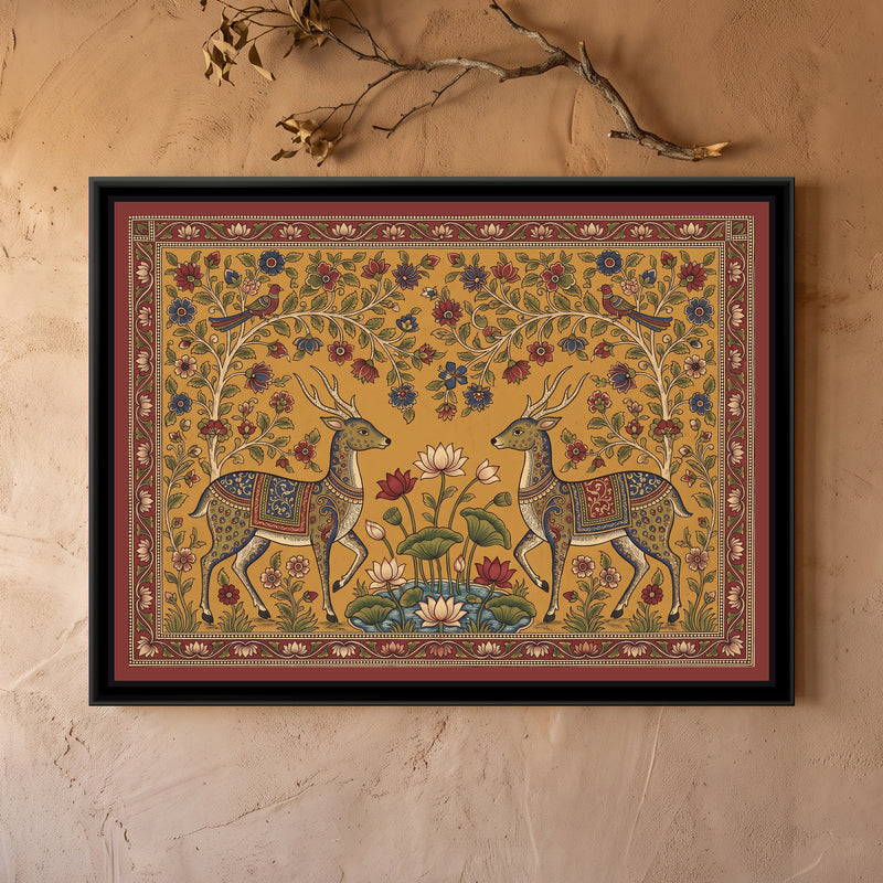 Kalamkari Painting – Deer Pair at a Lotus Pond - framed canvas print of two antlered deer with dotted coats and indigo and red patterned saddle cloths stepping toward each other on either side of a small blue lotus pond with pink, cream and red lotuses and broad green leaves, flowering trees arching over them with a red bird perched on each side, red, indigo and cream flowers scattered over a mustard ground, a deep red border of small cream flowers, hung on a wall