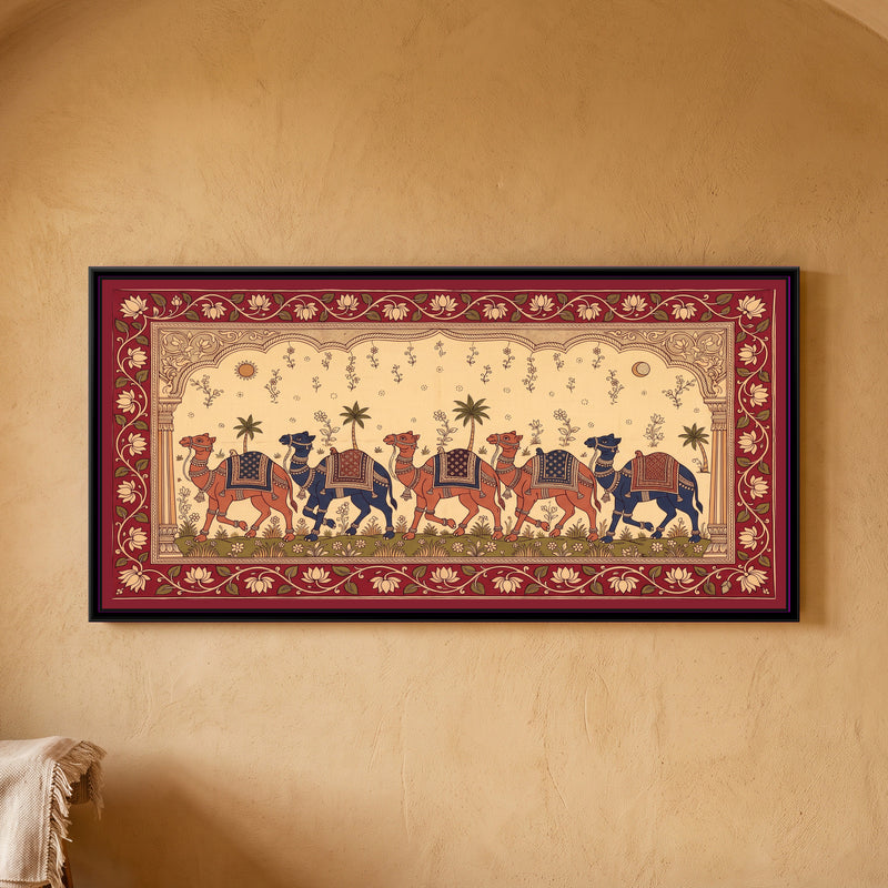 Kalamkari Painting – Camel Caravan Procession - framed canvas print of five camels, alternating terracotta red and indigo, walking in a line across a green meadow of small flowers, each with a patterned saddle cloth, tassels, bells and anklets, palm trees and flowering sprigs behind them, a sun on the left and a crescent moon on the right in a cream sky, a carved scalloped arch on two pillars, a deep red border of cream lotuses on a vine, hung on a wall