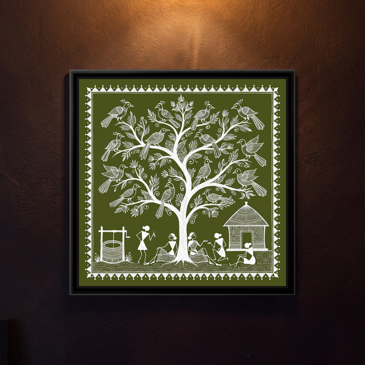 Warli Painting – Tree of Life with Birds – Olive Square - framed canvas print of a square Warli tree of life with a smooth white trunk and leafy curling branches holding sixteen large crested birds with patterned wings, a well with a winch on the left, a hut with spiral-patterned walls on the right, villagers sitting and chatting under the tree on a strip of grass, white line on an olive green ground inside a border of white triangles and dots, hung on a wall