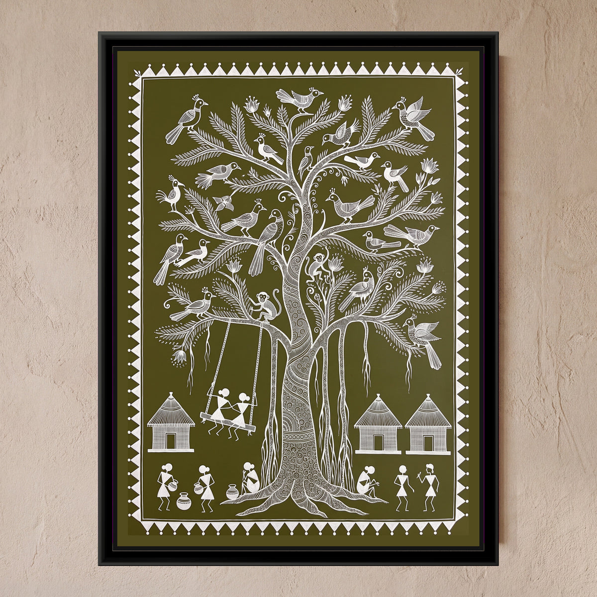 Warli Painting – Banyan Tree with a Swing - framed canvas print of a tall Warli banyan tree with a spiral-patterned trunk, hanging aerial roots and feathery branches full of crested birds and two monkeys, two figures sitting together on a wooden swing hung from a branch, three thatched huts, villagers carrying water pots and chatting along the bottom, white line on an olive green ground inside a border of white triangles and dots, hung on a wall